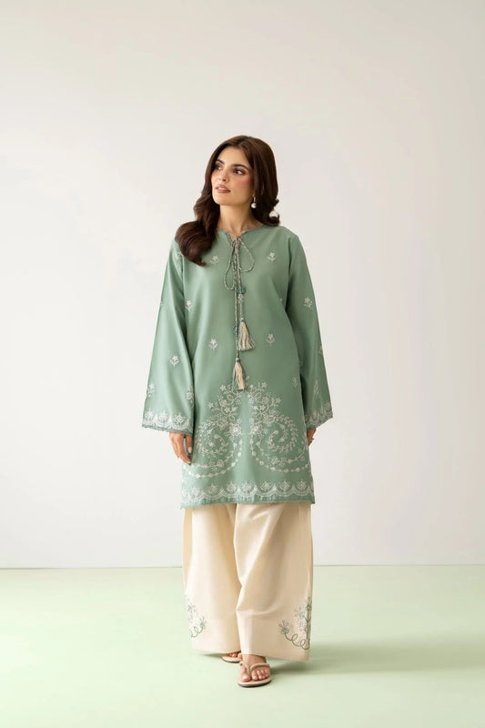 A woman modeling a sage green embroidered kurta with cream wide-leg pants, standing against a light neutral studio background.